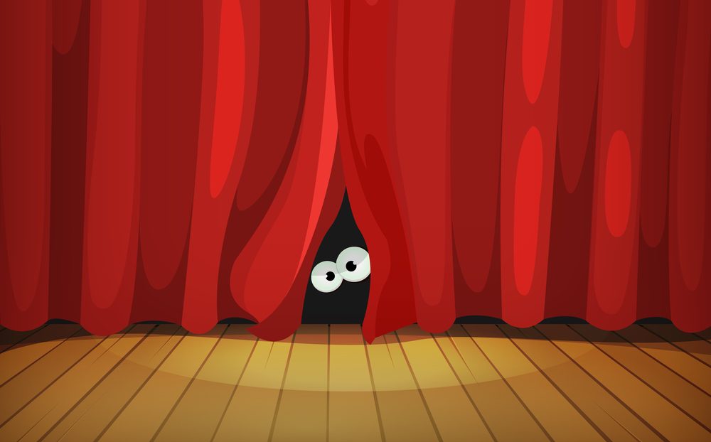 Eyes behind red curtains on wooden stage