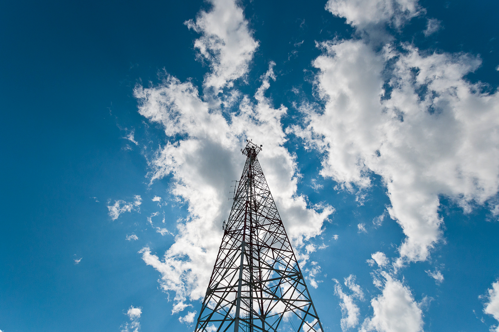 Cell phone tower against blue sky and fluffy clouds